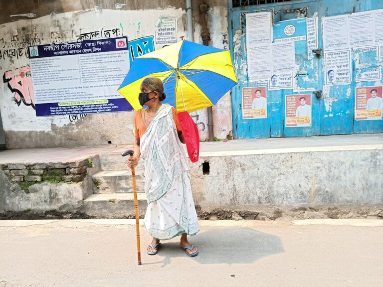 woman in white robe holding yellow umbrella walking on beach during daytime