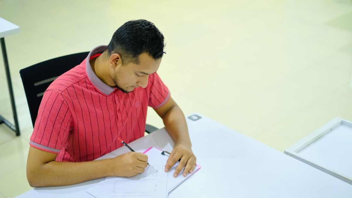 man in red and white striped crew neck t-shirt writing on white paper